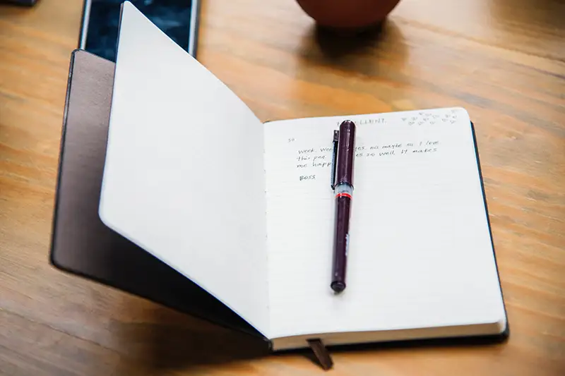 Notebook lays open on a desk with a pen resting on the pages