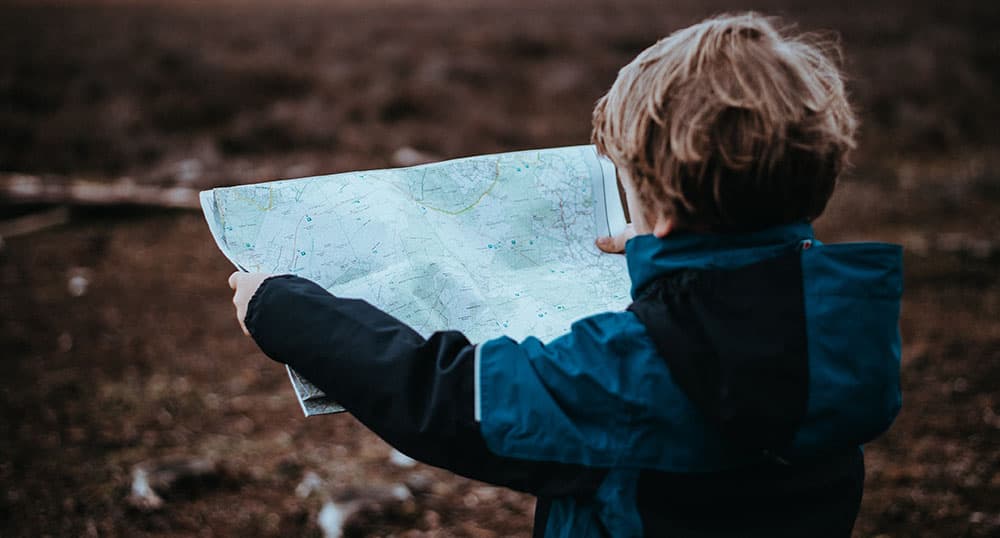 Child stands in a field, looking at a paper map