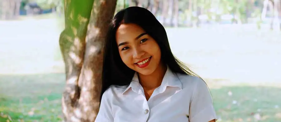 Young woman sits under a tree, smiling at the camera