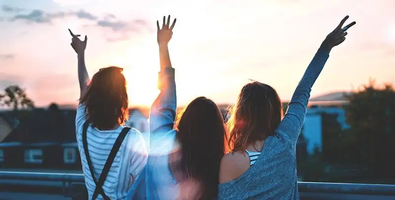 Three girls stand with hands in the air excitedly