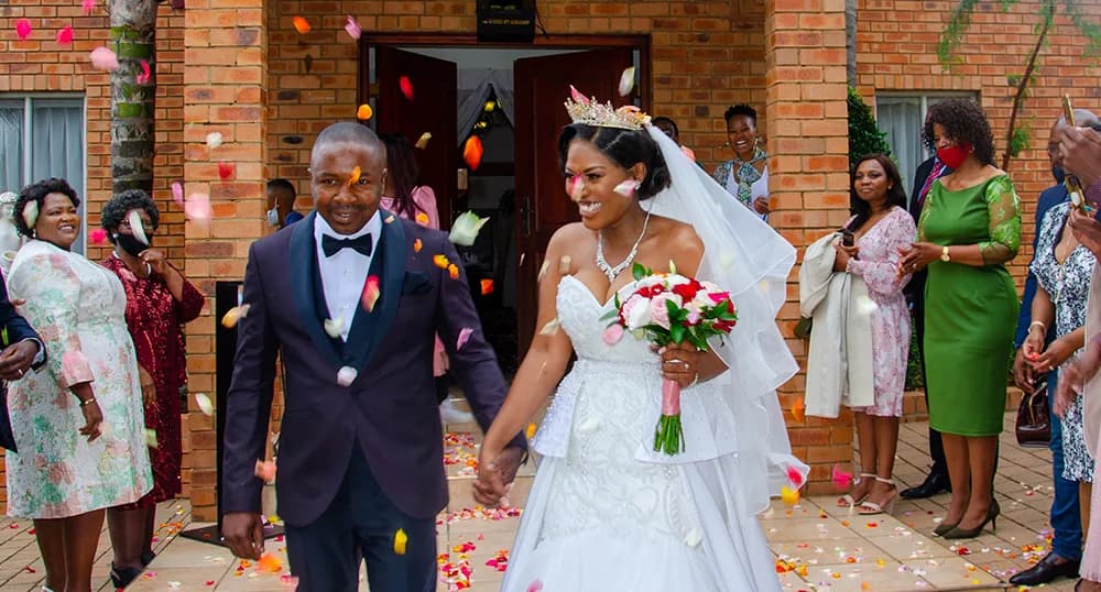 Bride and groom walk out of the building, guests throw confetti