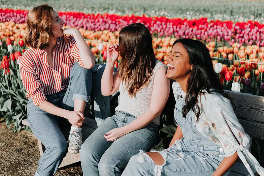 Three young women sit on a bench in tulip field