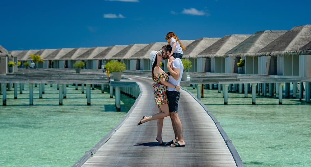 Family of three stands on a boardwalk near overwater bungalows