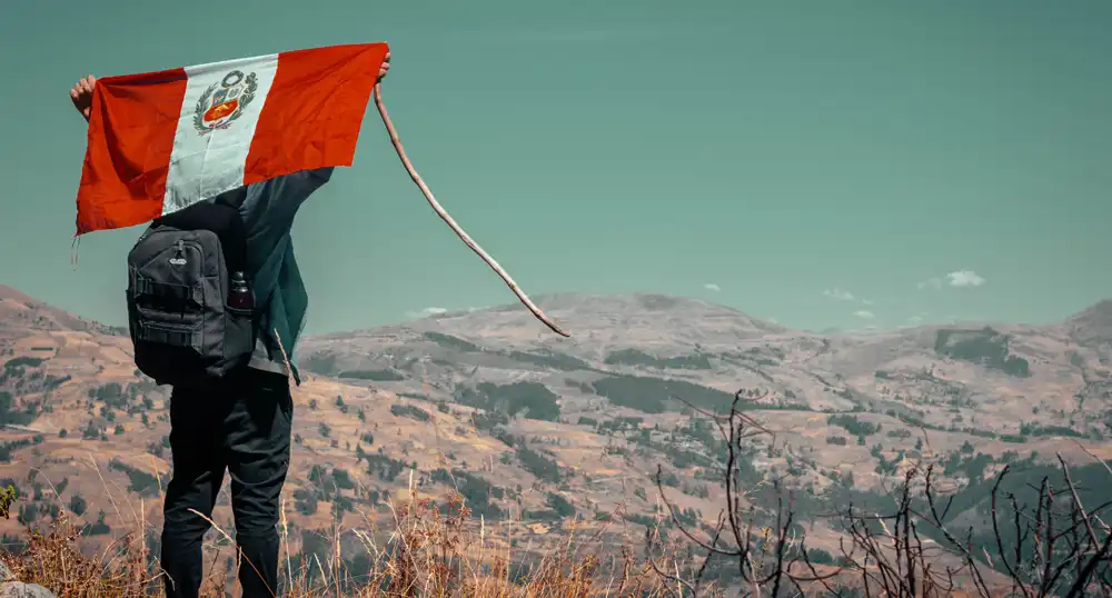 Man stands in the hills, holding up a Peruvian flag