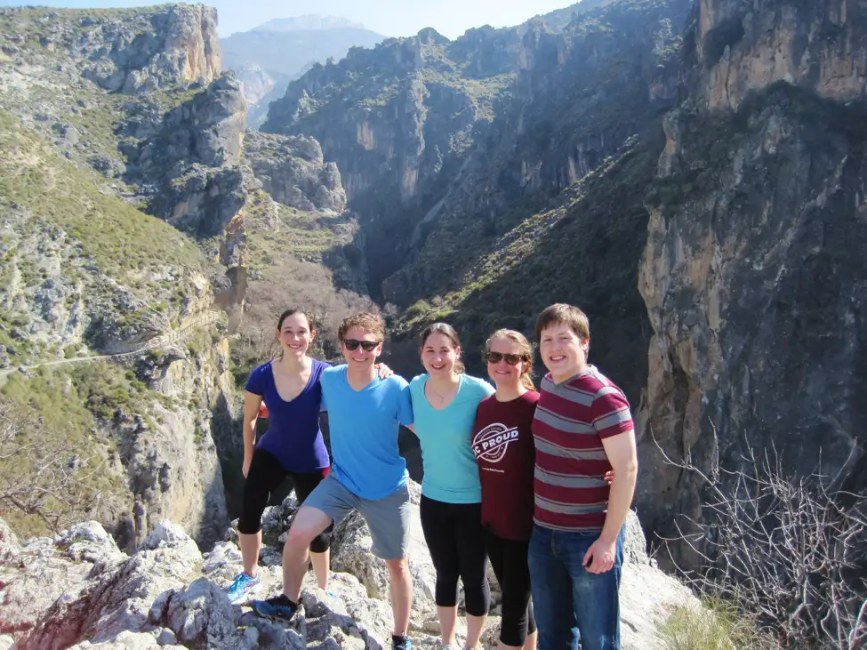 Five people pose in front of a cliff during hike