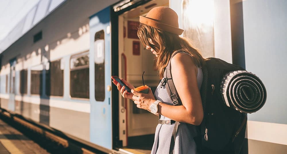 Woman looks at her phone while standing outside next to a train