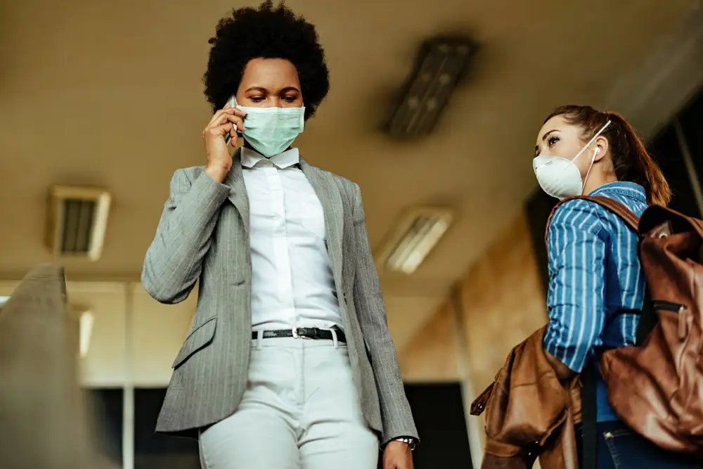 Two women passing each other in public with masks on.