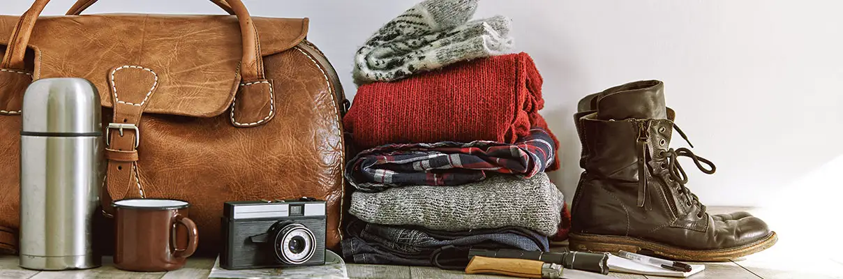 A suitcase, clothes, boots and cameral all waiting to be packed