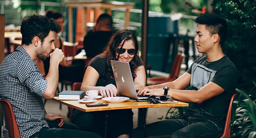 Three people sit around a cafe table, talking and working on homework