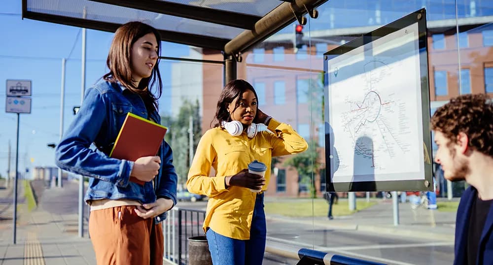 Three students sit and wait at a bus stop