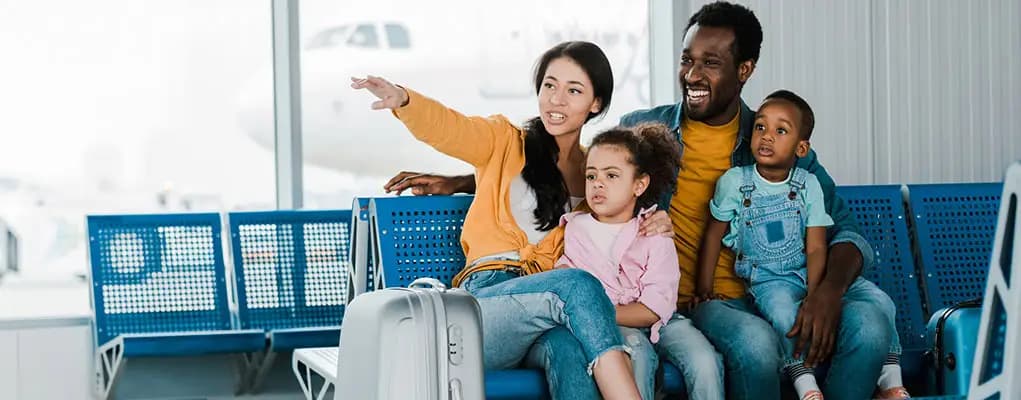 Happy family of 4 with 2 small children sit in an airport lounge