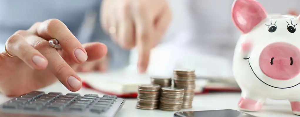 Person doing math on a calculator, surrounded by coins and piggy bank