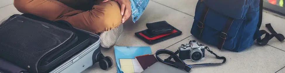 Suitcase, camera, backpack, and other items on the floor, waiting to be packed for vacation