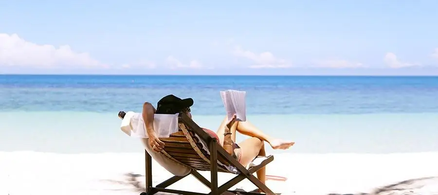 Woman lounges in a beach chair, reading a book on the beach